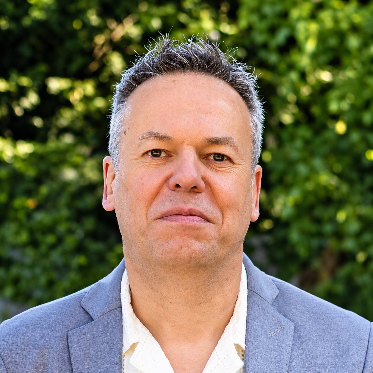 Marc Duren, développeur full stack, veste grise-bleue devant un feuillage vert